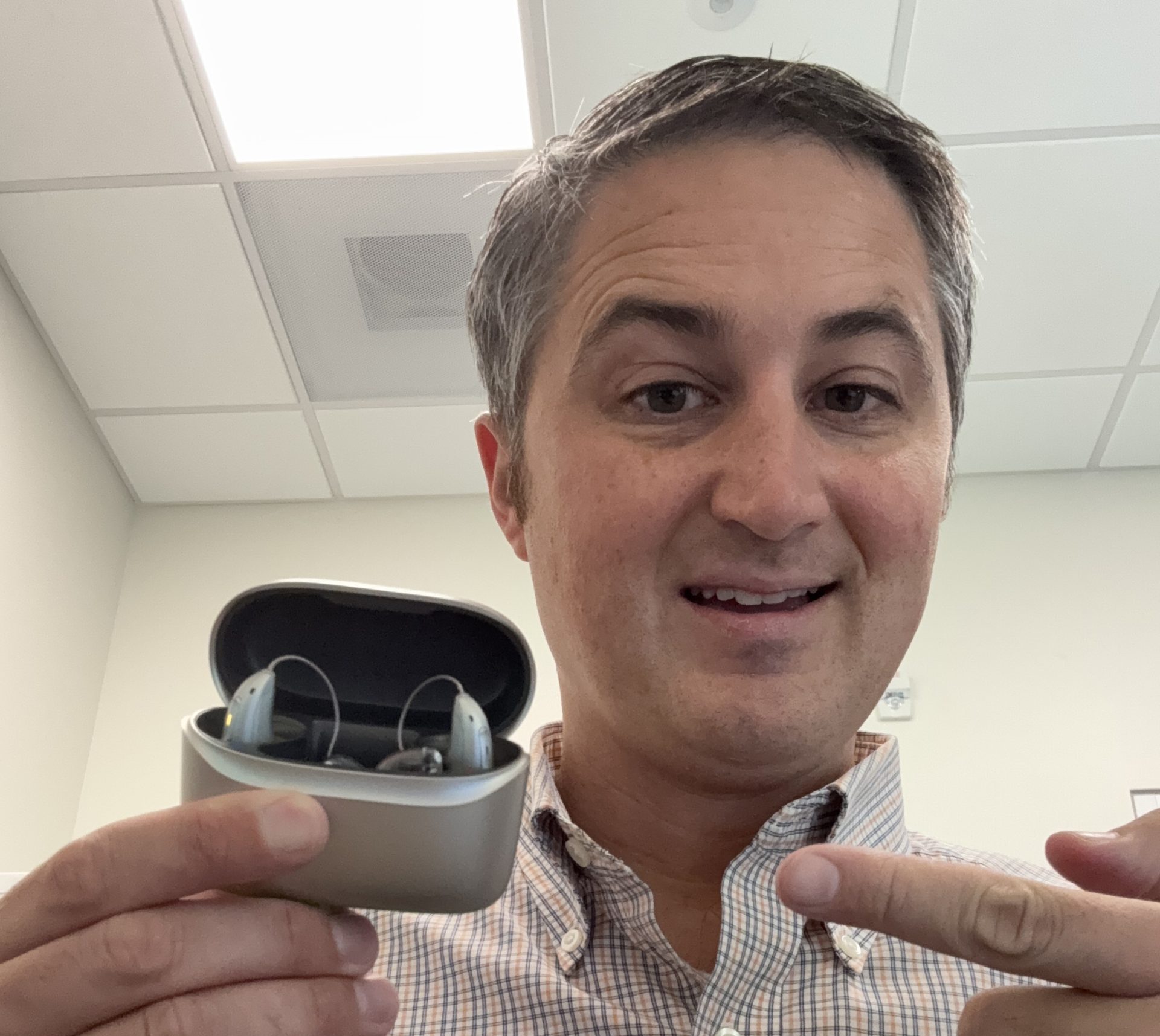 audiologist hold phonak audeo sphere hearing aids in their charger case with finger pointing to them